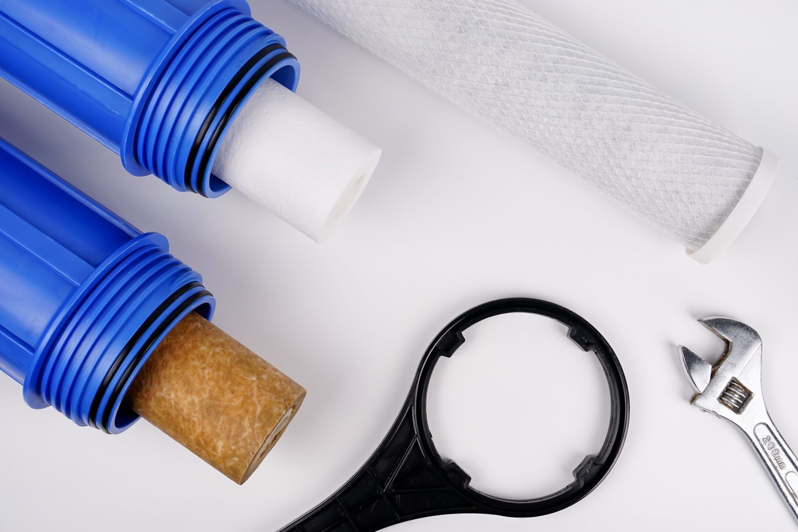 Filter housings, sediment and carbon cartridges, and service tools arranged on a white surface